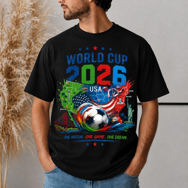 May include: Black t-shirt with a colorful graphic design for the 2026 World Cup in the USA. The design includes a soccer ball, the USA map, and the text "World Cup 2026 USA" and "One Nation. One Game. One Dream."
