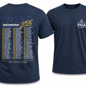 K&ouml;nnte beinhalten: Marineblaue T-Shirts mit dem PGA-Logo und Text. Ein Shirt zeigt den Text "PGA ARONIMINK 2026" mit einer Liste von Namen und Veranstaltungsdetails. Das andere Shirt hat ein kleineres Logo und den Text "2026 PGA ARONIMINK".