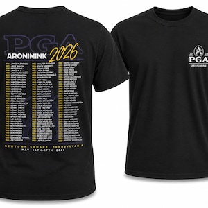 K&ouml;nnte beinhalten: Schwarze T-Shirts mit PGA-Logo und Eventdetails. Ein Shirt zeigt das PGA-Logo auf der Vorderseite. Das andere Shirt hat eine Liste von Namen und Veranstaltungsinformationen, einschlie&szlig;lich "ARONIMINK 2026" und "NEWTOWN SQUARE, PENNSYLVANIA".
