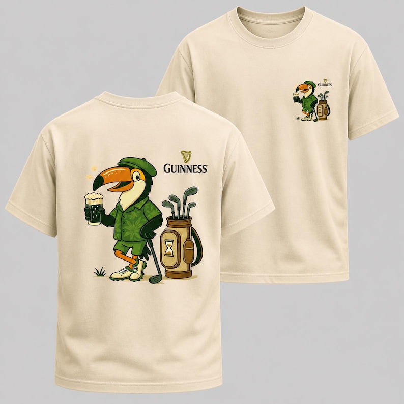 May include: Beige t-shirts with a Guinness-themed design. The front of the shirt features a cartoon toucan in a green outfit, holding a pint of beer and a golf club. The Guinness logo is also visible. The back of the shirt has the Guinness logo.