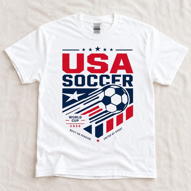 May include: White t-shirt with a graphic design featuring the text "USA SOCCER" in red and blue, a soccer ball, and the text "WORLD CUP 2026". The design includes stars and stripes.