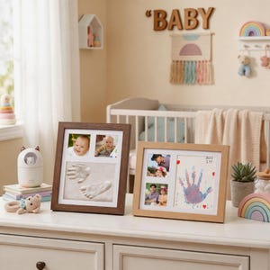 May include: Two rectangular picture frames sit on a white surface. The left frame is dark wood and contains two photos of a baby and a clay impression of a hand and foot. The right frame is light wood and holds two photos and a colorful handprint.