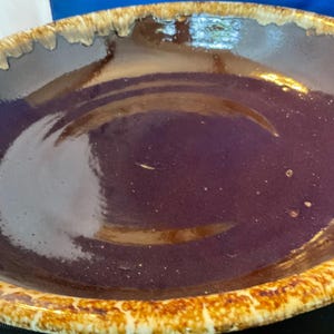 May include: A large, round, ceramic serving bowl with a deep purple interior and a textured, light brown rim. The rim has a speckled, aged appearance. The bowl is likely used for serving food.