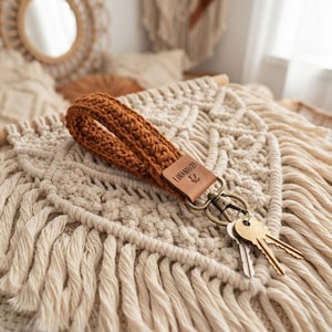 Peut inclure: Un porte-clés bracelet en crochet de couleur rouille avec une étiquette en cuir marron gravée du texte LINAMORI et d'un petit logo. Le bracelet est fixé à un mousqueton pivotant en métal couleur laiton retenant deux clés en métal argenté.