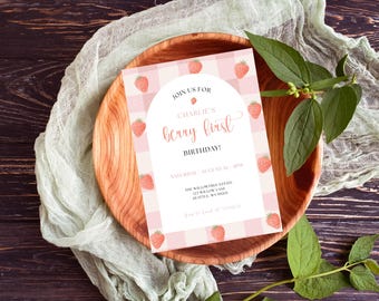 May include: A birthday invitation with a strawberry theme. The invitation features a pink and white gingham pattern and strawberry illustrations. Text reads "Join us for Charlie's berry first birthday!" The invitation is on a wooden plate with a green cloth and leaves.