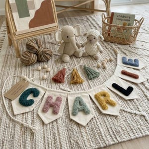 May include: A children's room decor scene featuring a banner spelling "CHARLIE" with colorful, textured letters.  Also present are crochet elephant and lamb toys, yarn balls, tassels, and a children's song book in a basket.