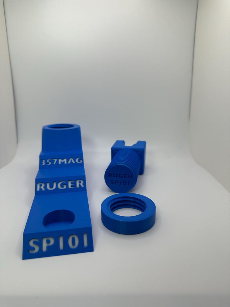 May include: Blue 3D-printed accessories, including a stepped stand with "357MAG", "RUGER", and "SP101" text, a cylindrical piece with "RUGER SP101", and a circular threaded component. The items are set against a white background.