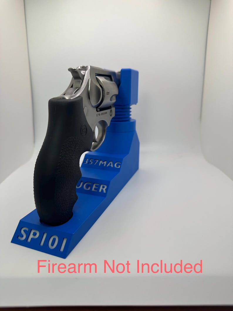 May include: A stainless steel revolver with a black grip is displayed on a blue stand. The stand has the text "357MAG", "RUGER", and "SP101". The text "Firearm Not Included" is at the bottom.
