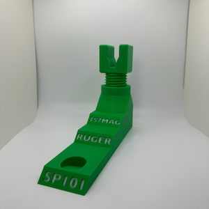 Op de afbeelding: Een felgroene, 3D-geprinte wapenstandaard met de tekst "SP101", "RUGER" en "357MAG". De standaard heeft een trapsgewijs ontwerp met een cirkelvormig gat en een U-vormige bovenkant. De standaard is ontworpen om een ​​vuurwapen vast te houden.