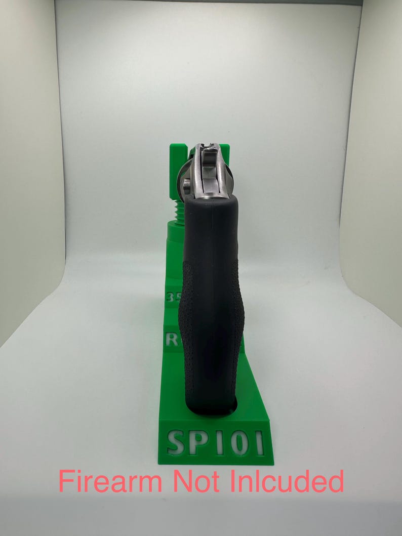 May include: A black handgun with a silver cylinder is held in a bright green stand. The stand has the text "SP101" and "Firearm Not Included" in pink. The stand is designed to hold the handgun.