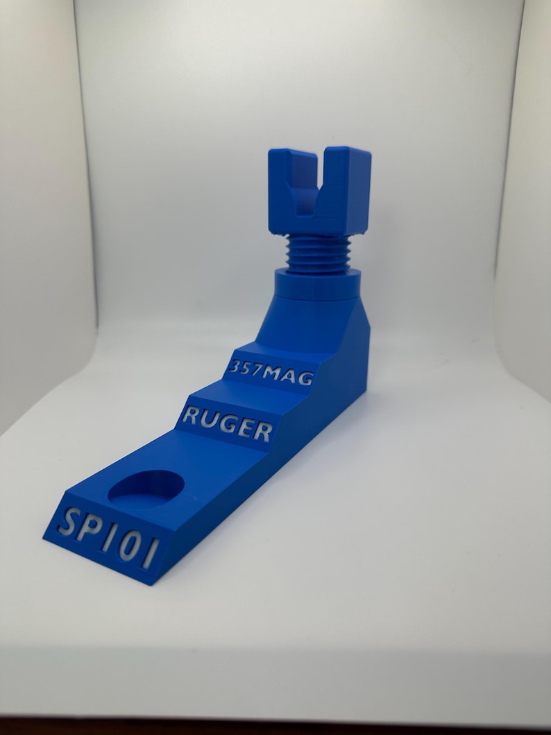 May include: A vibrant blue 3D-printed object with the text "SP101", "RUGER", and "357MAG". The object has a stepped design with a hole and a threaded section. The top features a U-shaped component.