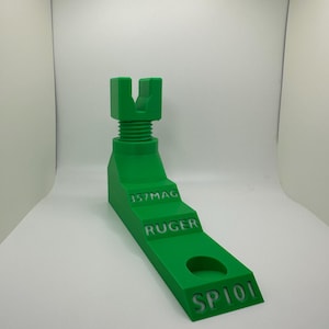 May include: A bright green, 3D-printed firearm stand. The stand features a stepped design with the engraved text "357MAG", "RUGER", and "SP101". It has a threaded top section and a circular hole. The stand is designed to hold a firearm.