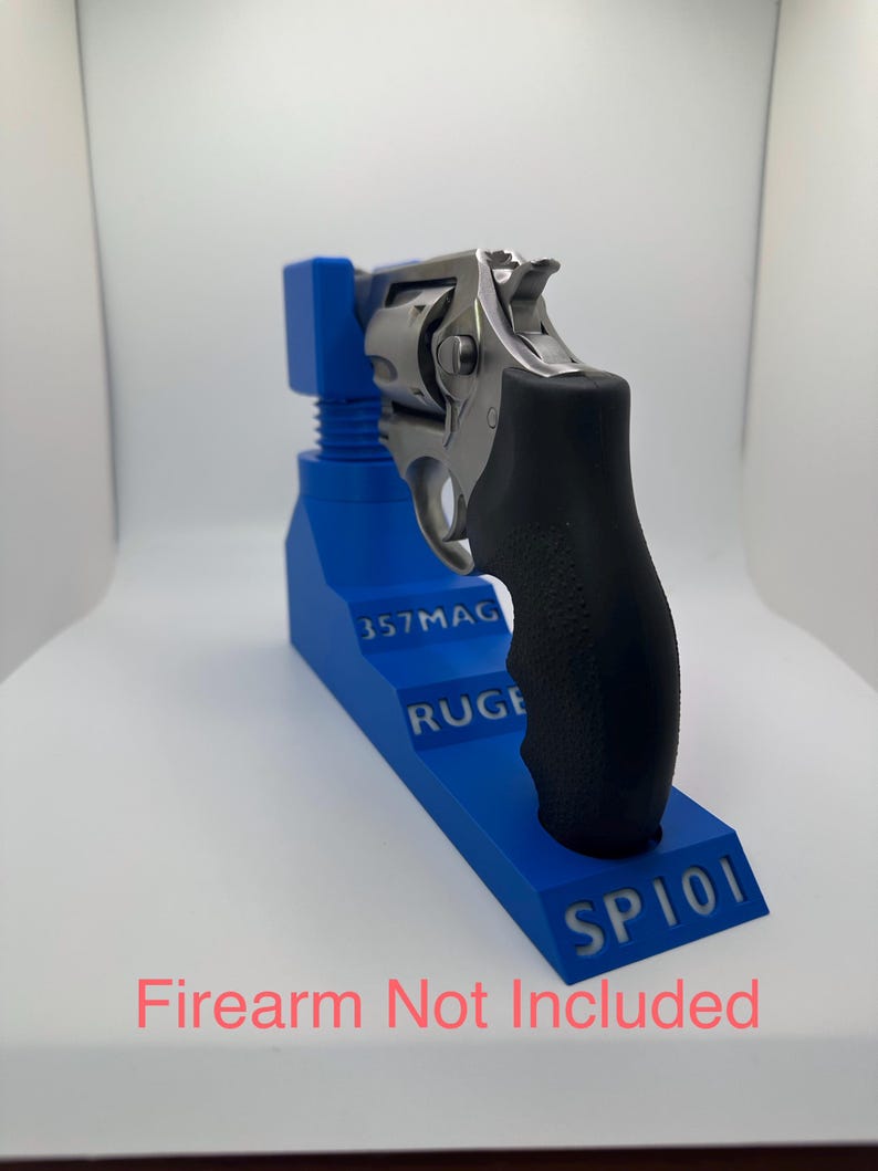 May include: A blue firearm stand with the text "357MAG RUGE SP101". A silver and black handgun rests on the stand. The text "Firearm Not Included" is at the bottom.