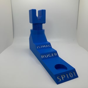 May include: A blue 3D-printed tool with the text "357MAG", "RUGER", and "SP101". The tool has a stepped design with a threaded section and a U-shaped top. It is designed for a specific firearm model.