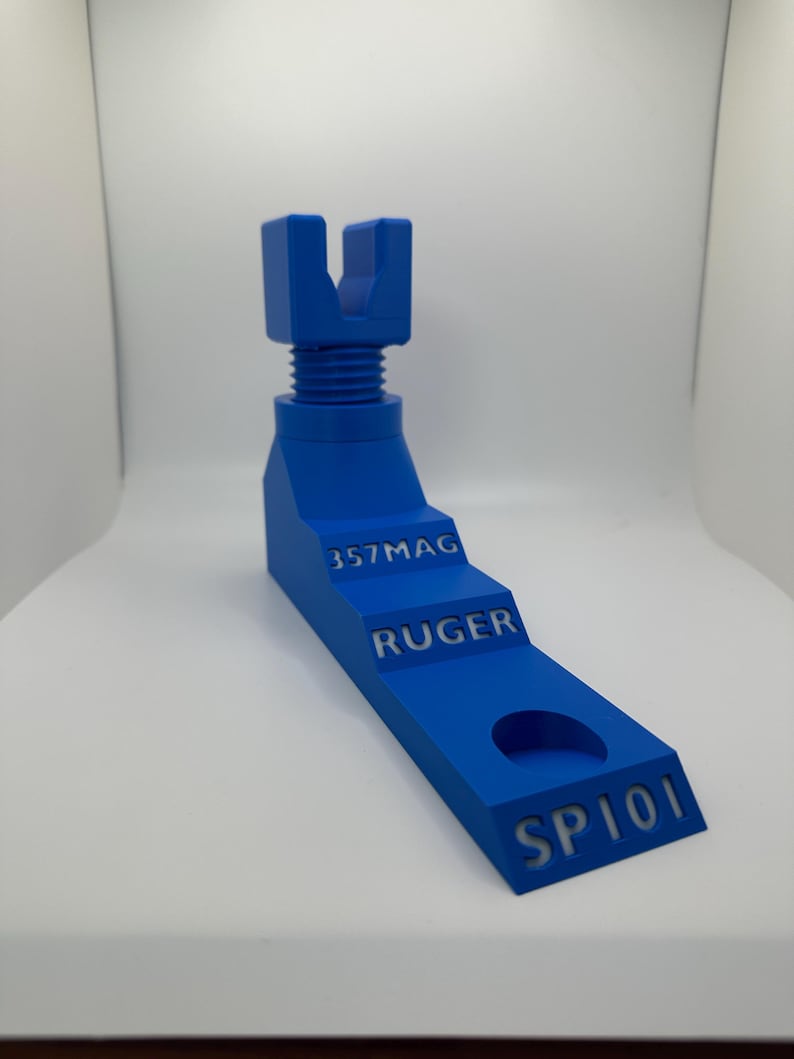 May include: A blue 3D-printed tool with the text "357MAG", "RUGER", and "SP101". The tool has a stepped design with a threaded section and a U-shaped top. It is designed for a specific firearm model.