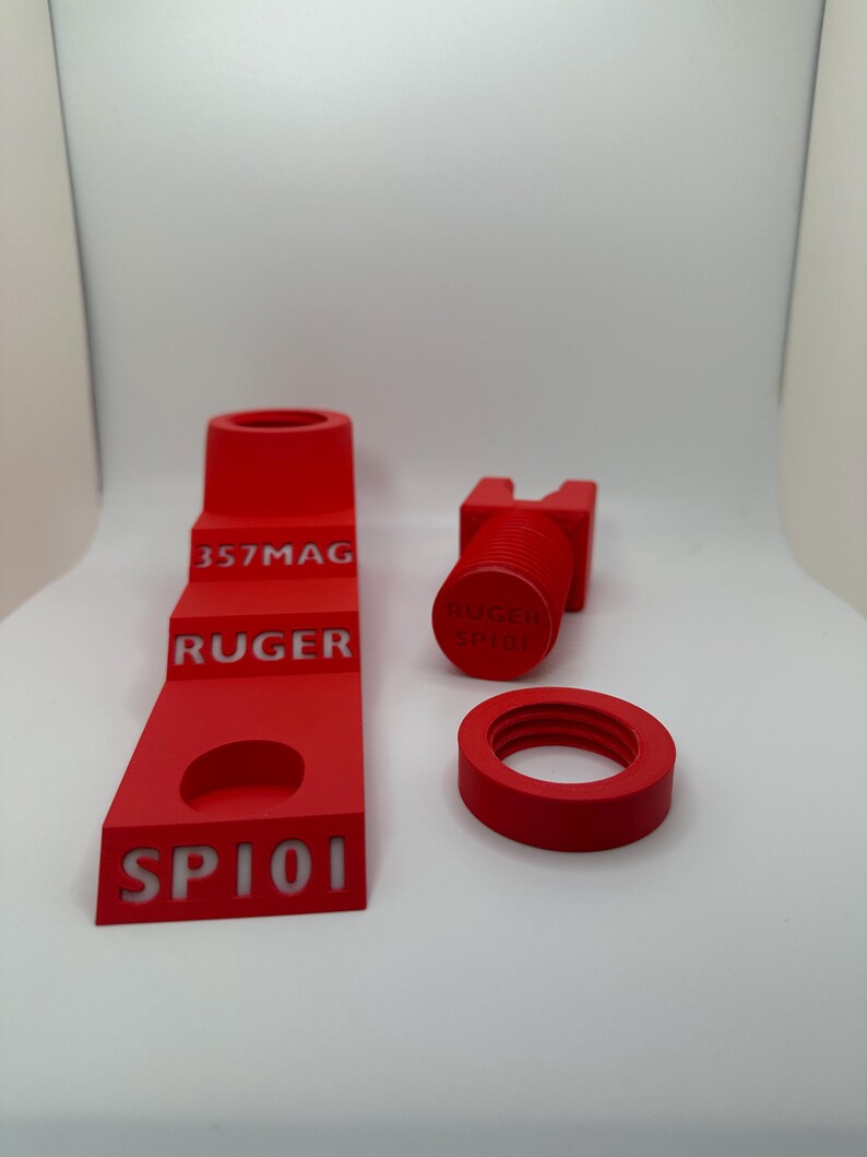 May include: A set of four bright red 3D-printed accessories. The set includes a stepped stand with "357MAG", "RUGER", and "SP101" text, a threaded cylinder with "RUGER SP101" text, and a ring.