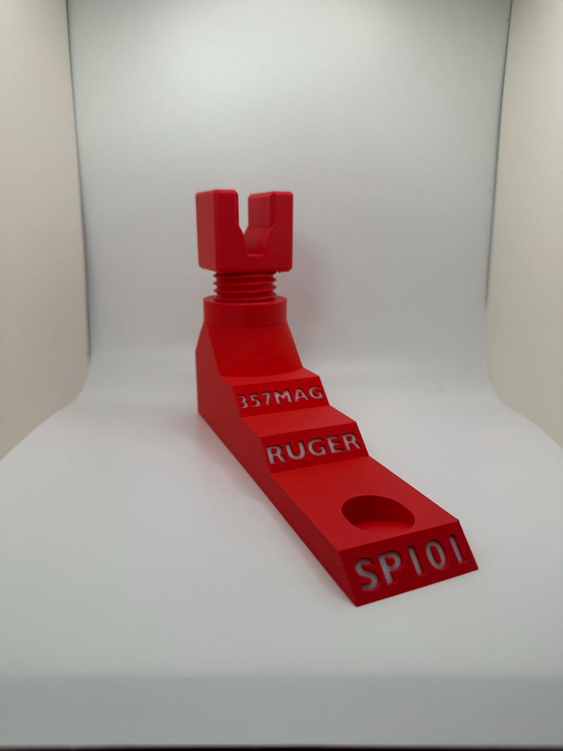 May include: A bright red, 3D-printed object with a stepped design. The object has a threaded top section and text that reads "357MAG", "RUGER", and "SP101". It features a circular hole near the base.