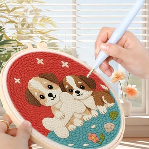 Può includere: Telaio da ricamo ovale con sfondo rosso con due disegni di cuccioli. I cuccioli sono marroni, bianchi e beige. Un ago da punzonatura viene utilizzato per creare il disegno. Il telaio è color crema.