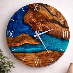 May include: A round wall clock featuring a natural wood grain face with a vibrant blue epoxy resin river running through the center. The clock has white Roman numerals at the twelve, three, six, and nine o'clock positions and white hands.