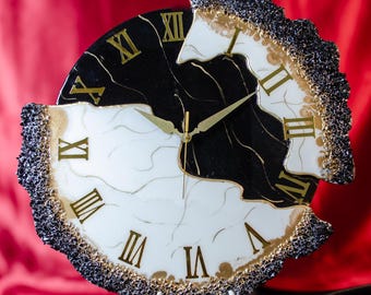 Può includere: Un orologio decorativo con un design a effetto marmo bianco e nero. Il quadrante presenta numeri romani dorati e lancette dorate. L'orologio ha un bordo strutturato nero e oro ed è esposto su un piccolo supporto.