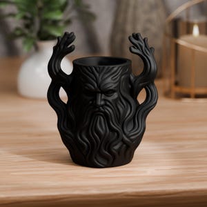 Könnte beinhalten: Eine mattschwarze Keramiktasse mit einem geformten Gesichts- und Bartdesign. Die Tasse hat baumartige Griffe und eine detaillierte Darstellung eines bärtigen Gesichts. Die Tasse ist etwa 13 cm hoch.