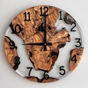 Peut inclure: Une horloge murale ronde composée d'une tranche de bois naturel aux bords irréguliers incrustée dans de la résine transparente. Le cadran présente des chiffres arabes noirs de 1 à 12 et trois aiguilles noires fixées au centre du bois.