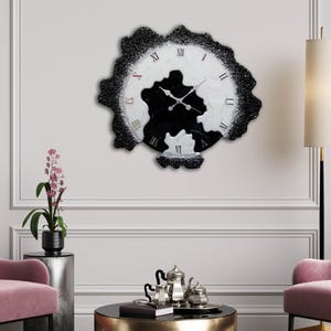 Puede incluir: Un reloj de pared decorativo con un diseño único. El reloj presenta una esfera veteada en blanco y negro con números romanos rojos. El borde exterior del reloj es de un material negro texturizado, que añade un toque moderno al diseño.
