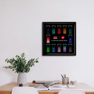 Può includere: Opera d'arte incorniciata con sfondo nero, con disegni rettangolari colorati che rappresentano i team di Formula 1. Il testo "IT'S LIGHTS OUT AND AWAY WE GO!" è stampato in bianco. L'opera è esposta su una parete bianca.