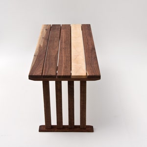 May include: A wooden table with a walnut and maple top. The table has a simple, modern design with a rectangular top and four legs.