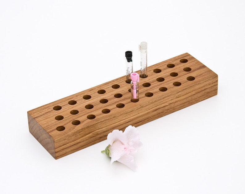 May include: A wooden organizer with multiple holes for storing small perfume bottles. Three perfume bottles are in the organizer, one is pink, one is black, and one is clear.