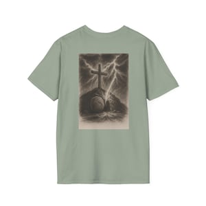 May include: Sage green t-shirt featuring a sepia-toned graphic. The graphic depicts a cross atop a hill, with a tomb and lightning in the background. The shirt is a classic crew neck style.
