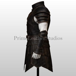 Pode incluir: Uma armadura de couro castanho escuro com ombreiras, protetores de bra&ccedil;o e uma saia. A armadura tem um acabamento envelhecido e &eacute; detalhada com rebites e um cinto. O texto "Prime Leather Studios" &eacute; vis&iacute;vel.
