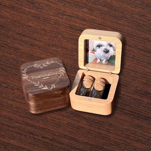 May include: Wooden keepsake box with a photo of a dog inside the lid. The box is open, revealing two small glass vials with cork stoppers. The lid of the box features the word "Marshmellow" inside a heart-shaped design.
