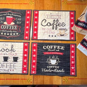 May include: Four black and white coffee-themed placemats with red and white stars around the border. The placemats feature different sayings about coffee, including "You can't buy happiness, but you can buy coffee", "Hello Coffee, my old friend", "Coffee doesn't ask silly questions", and "Oh look it's coffee o'clock".