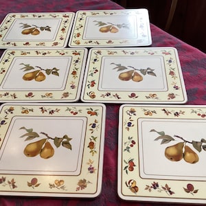 Puede incluir: Juego de seis manteles individuales cuadrados. Cada uno presenta una imagen central de dos peras amarillas en una rama con hojas verdes. El borde tiene un fondo crema con un diseño floral y de frutas.