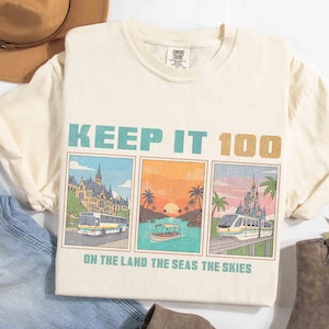 Puede incluir: Camiseta color crema con el texto "KEEP IT 100" en turquesa y dorado. Debajo, tres imágenes rectangulares que representan un autobús, un barco y un tren. El texto "ON THE LAND THE SEAS THE SKIES" está debajo.