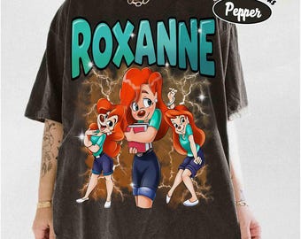 May include: Dark gray t-shirt featuring the name "Roxanne" in teal lettering above a cartoon graphic of a woman with red hair, wearing a teal top and blue shorts. The shirt has a vintage look with the words "Comfort Colors Pepper" in a black oval.