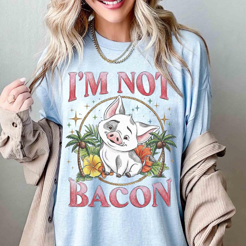 Puede incluir: Camiseta azul claro con el texto rojo "I'M NOT BACON". El dise&ntilde;o presenta un cerdo de dibujos animados sonriente, rodeado de flores tropicales y palmeras. El cerdo tiene manchas blancas y negras.