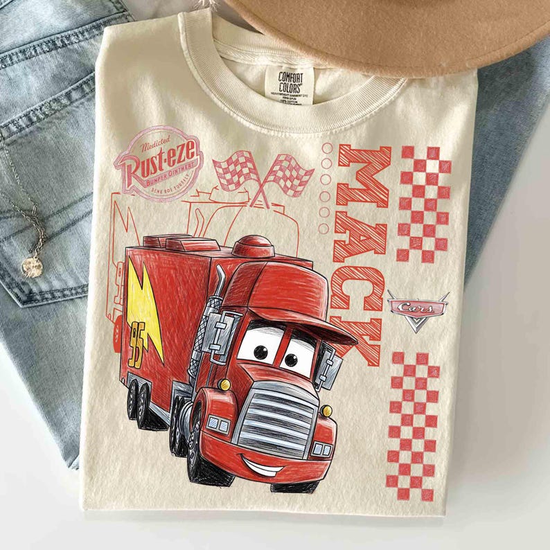 May include: Cream-colored t-shirt featuring a red cartoon illustration of Mack the truck from the movie Cars. The shirt also has the words "Mack" and "Rust-eze" printed on it, along with checkered flags and the number 95.