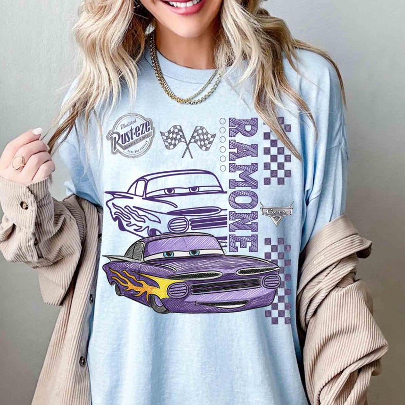 May include: Light blue long-sleeve shirt featuring a graphic of the character Ramone from the movie Cars. The design includes two cartoon cars, the name "Ramone", checkered flags, and the Rust-eze logo. The shirt has a relaxed fit.