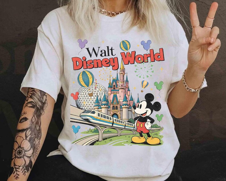Puede incluir: Camiseta blanca con un gr&aacute;fico colorido de Walt Disney World. El dise&ntilde;o incluye el logotipo del parque, un castillo, Mickey Mouse, un monorra&iacute;l y globos. La camiseta tiene mangas cortas y cuello redondo.
