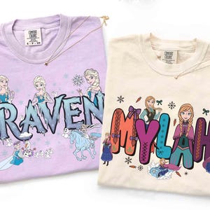 Puede incluir: Dos camisetas Comfort Colors, una lavanda y otra crema, cada una con un dise&ntilde;o gr&aacute;fico. La camiseta lavanda dice "Raven" con una ilustraci&oacute;n de princesa. La camiseta crema dice "Mylah" con una ilustraci&oacute;n de princesa.