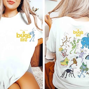 May include: White t-shirt with the words "a bug's life" in yellow and a blue ant illustration. The back of the shirt showcases colourful cartoon bug characters, including a blue elephant-like bug and a green grasshopper.