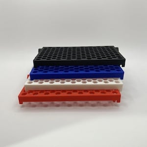 May include: A stack of four rectangular storage trays featuring a uniform hexagonal grid pattern. The trays are colored black, blue, white, and red from top to bottom. Each tray has a flat surface with numerous small circular openings.