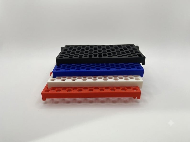 May include: A stack of four rectangular storage trays featuring a uniform hexagonal grid pattern. The trays are colored black, blue, white, and red from top to bottom. Each tray has a flat surface with numerous small circular openings.