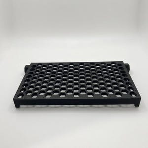 May include: A rectangular black tray featuring a repeating honeycomb pattern across its surface. The tray has a flat top with open hexagonal cutouts and short, sturdy legs at each corner, providing a raised structure for the object.