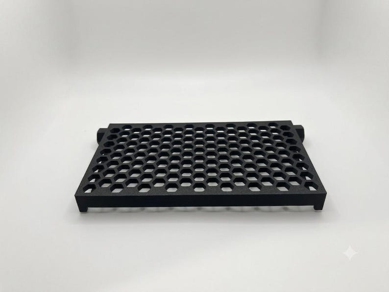 May include: A rectangular black tray featuring a repeating honeycomb pattern across its surface. The tray has a flat top with open hexagonal cutouts and short, sturdy legs at each corner, providing a raised structure for the object.