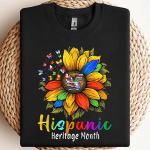 May include: Black sweatshirt with a vibrant sunflower design celebrating Hispanic Heritage Month. The sunflower incorporates various colours and flags. The text "Hispanic Heritage Month" is displayed in a rainbow of colours.