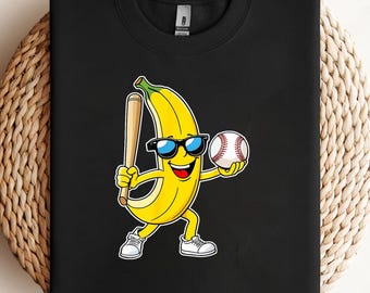 May include: Black sweatshirt with a cartoon banana character. The banana wears sunglasses, holds a baseball bat and a baseball. The banana is yellow with a green stem, wearing white trainers, and has a smiling face. The baseball is white with red stitching.