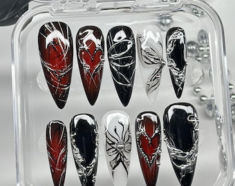 May include: A set of ten almond-shaped press-on nails arranged in a clear plastic case. The nails feature a color palette of deep red, black, and white, decorated with raised silver metallic 3D liquid-style accents, heart motifs, and fine lines.